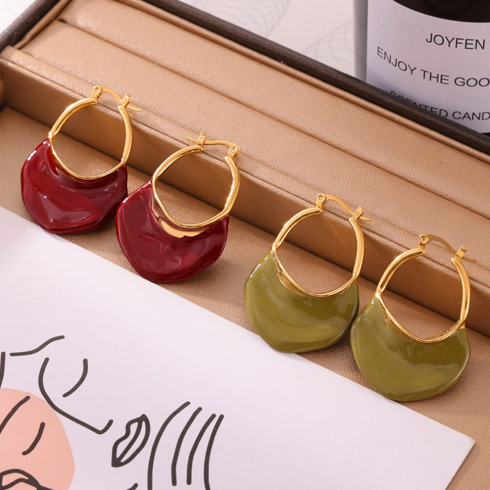 Gold calypso camille hoop earrings with red and green circular pendants on a beige surface.