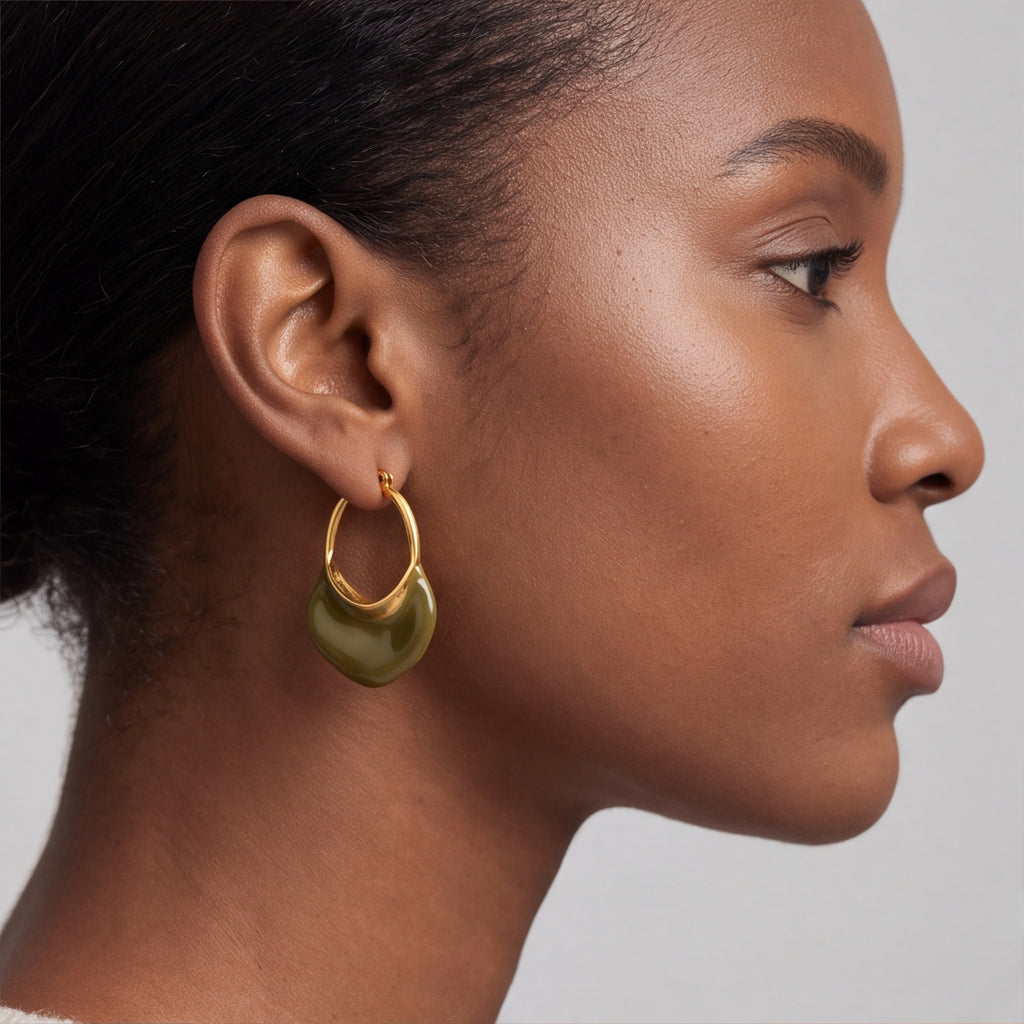 A close-up side profile of a model wearing a gold calypso camille hoop earring with a large, polished olive green crescent drop pendant.