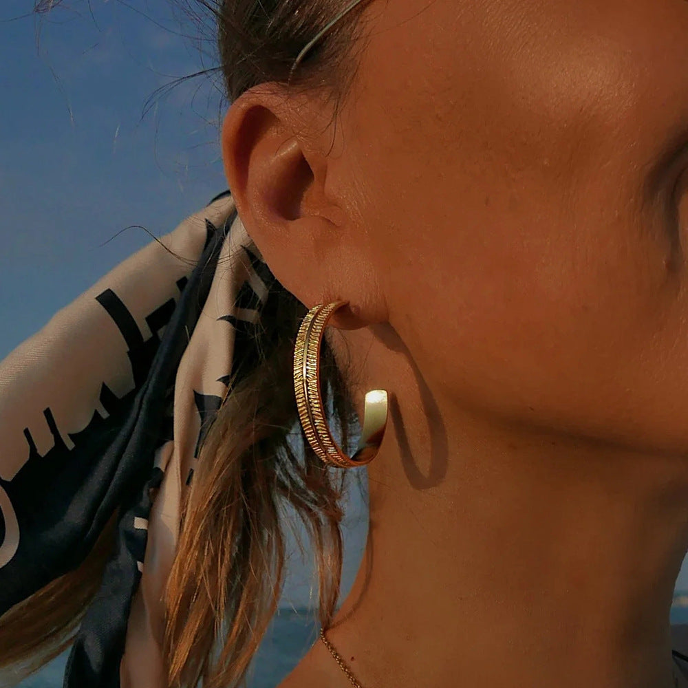 Close-up of a person wearing gold hoop earrings with a blurred background