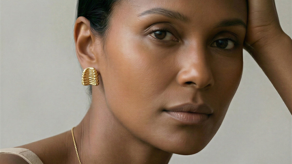 Woman wearing gold earrings and necklace against a neutral background