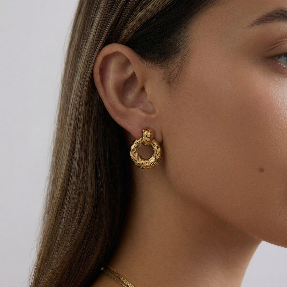 Close-up of a person wearing gold hoop earrings with a neutral background
