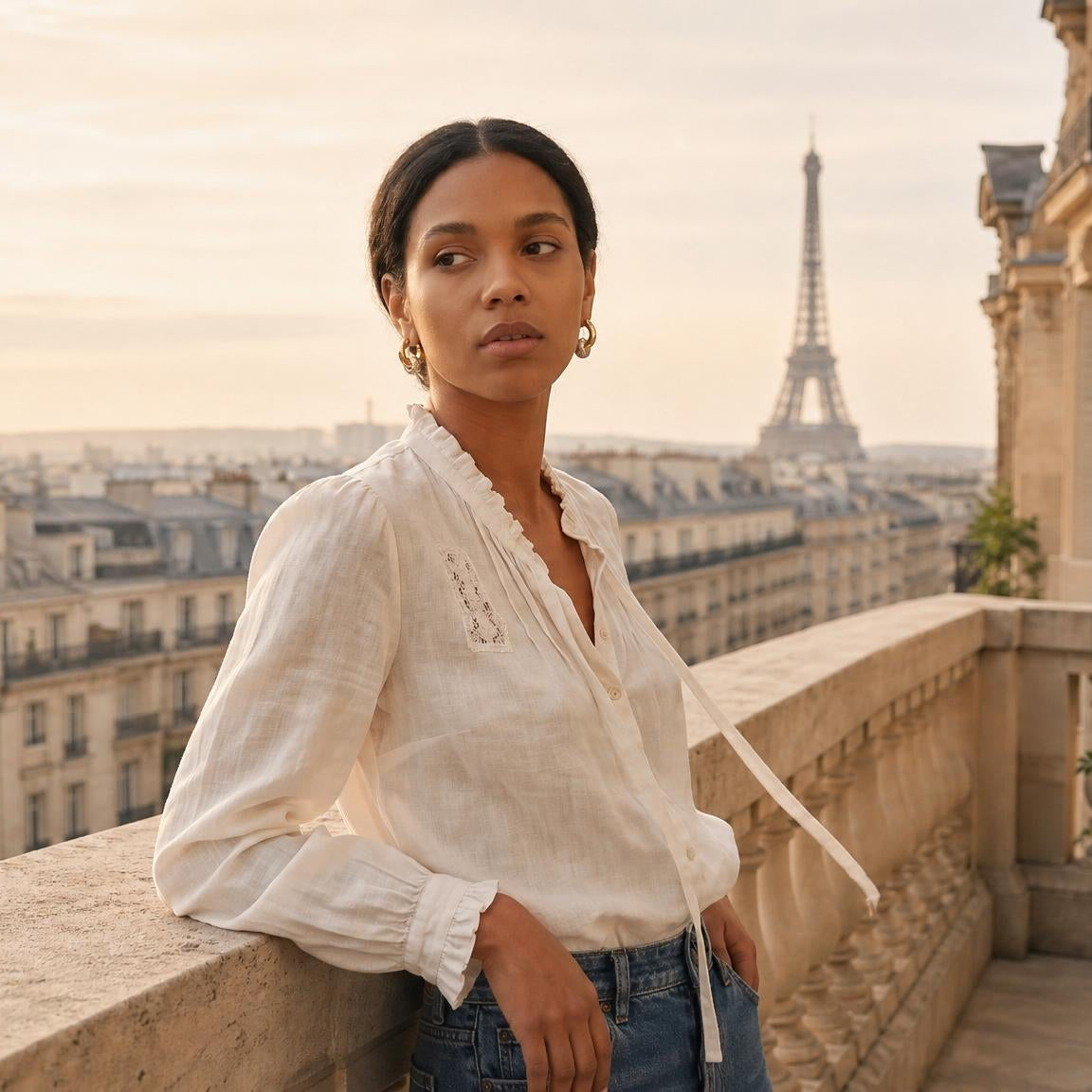 Woman standing on a balcony with the Eiffel Tower in the background wearing amethyst & sable's luma halo drop earrings.